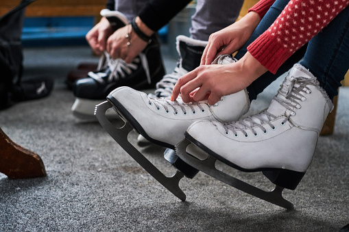 Young couple preparing to a skating. Close-up photo of their hands tying shoelaces of ice hockey skates